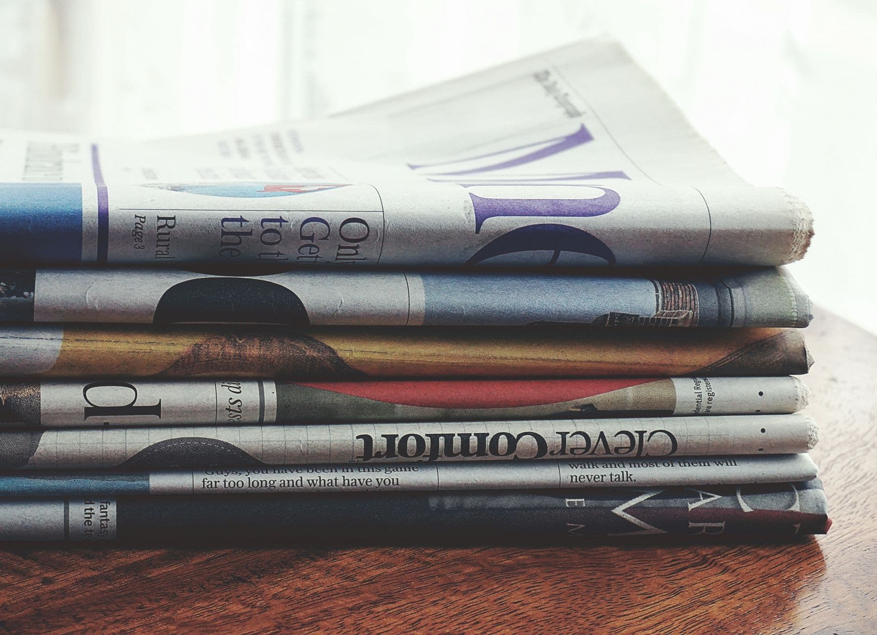 A stack of folded newspapers placed on a wooden table, symbolizing news and information.